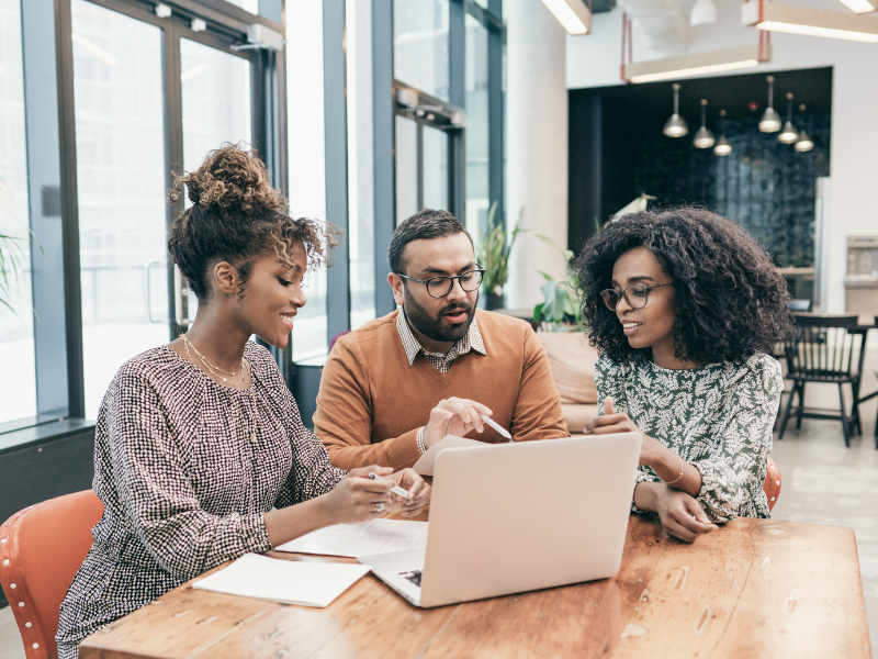 Real estate team of one man and two women meeting at table with computer on it