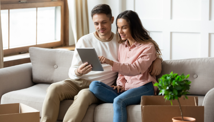 Couple sitting on couch looking at tablet with empty boxes around them. 