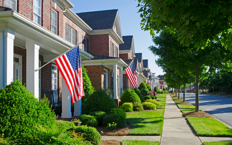 Row of brick homes with American flags hanging out front and green landscaping.