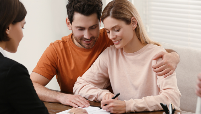 Man with arm around woman while she signs house documents. 