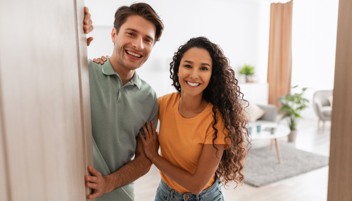 Couple opening door to greet guests into home. 